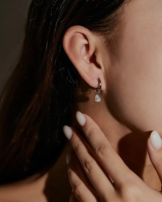 Pendientes de Aro de Moissanita Talla Pera en Plata 925 - llevados en la oreja de una modelo, con la mano cerca de la cara