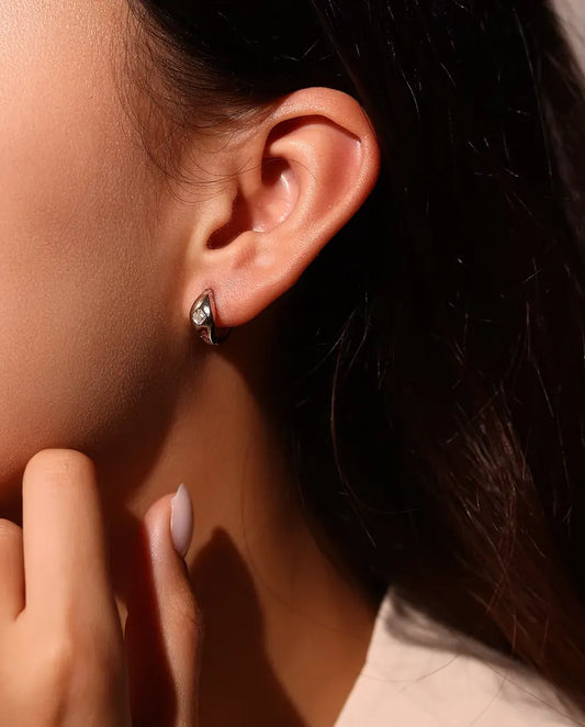 Pendientes de Aro Huggie de Moissanita Talla Asscher en Plata 925 - llevados en la oreja de una modelo, con la mano cerca de la cara
