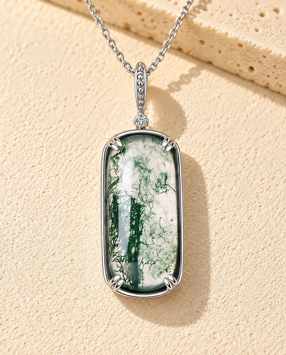 Collar de Ágata Musgosa con Colgante Rectangular en Plata 925 - sobre una superficie clara con textura junto a un bloque de travertino