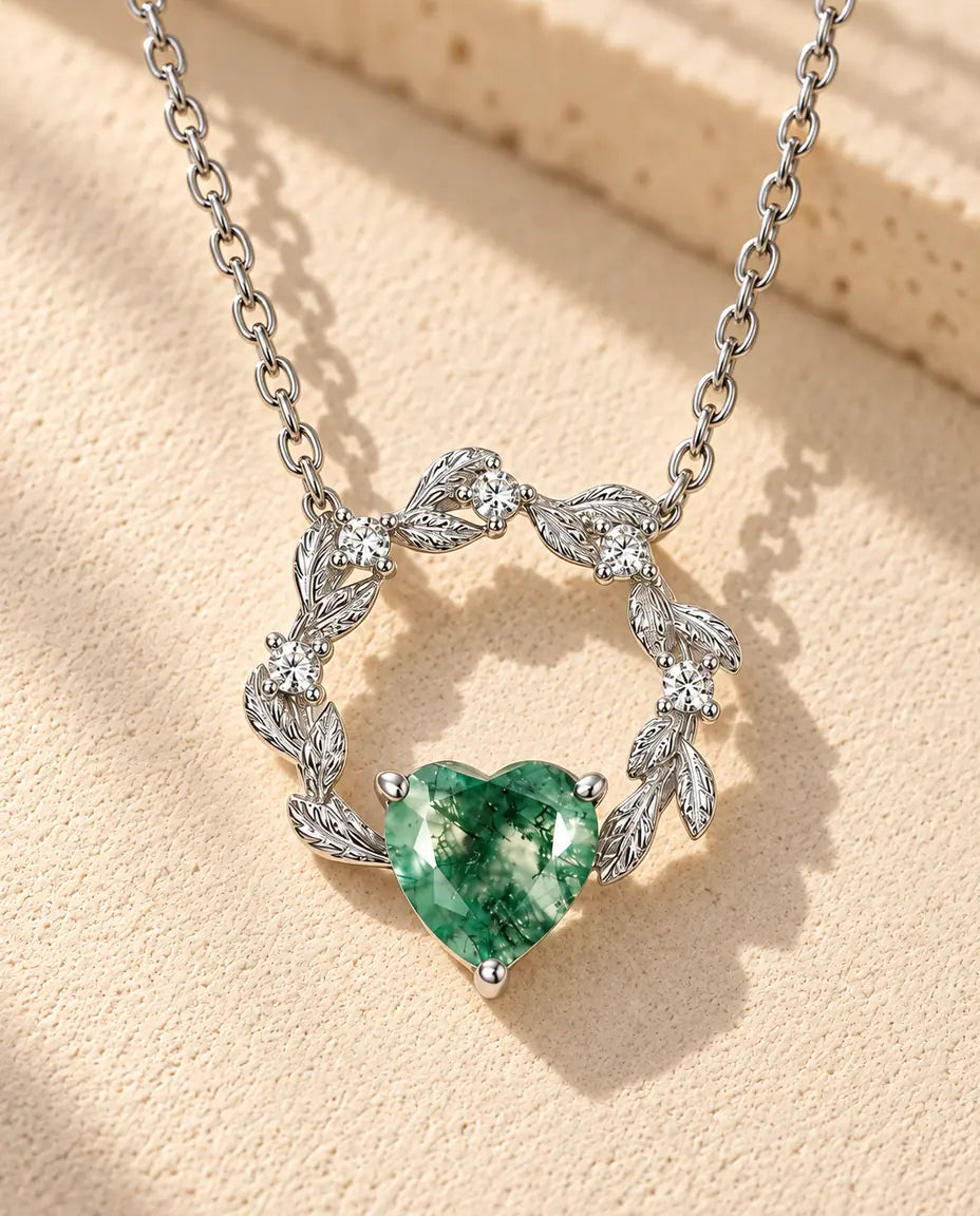 Collar de Corazón de Ágata Musgosa en Plata 925 - sobre una superficie clara con textura junto a un bloque de travertino
