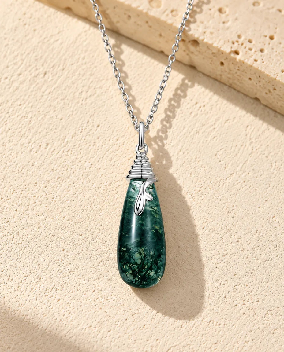 Collar de Ágata Musgosa en Forma de Gota en Plata 925 - sobre una superficie clara con textura junto a un bloque de travertino