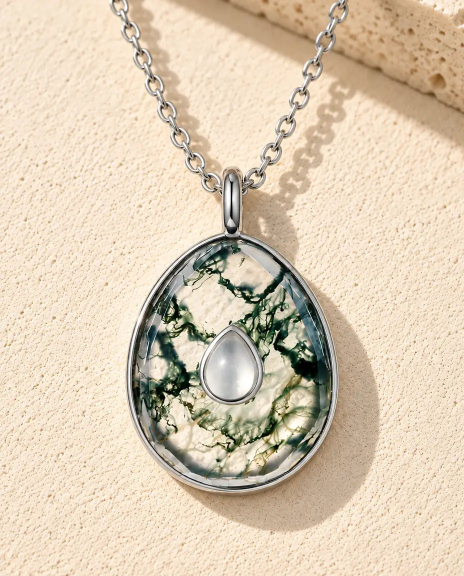 Collar de Ágata Musgosa en Forma de Huevo en Plata 925 - sobre una superficie clara con textura junto a un bloque de travertino