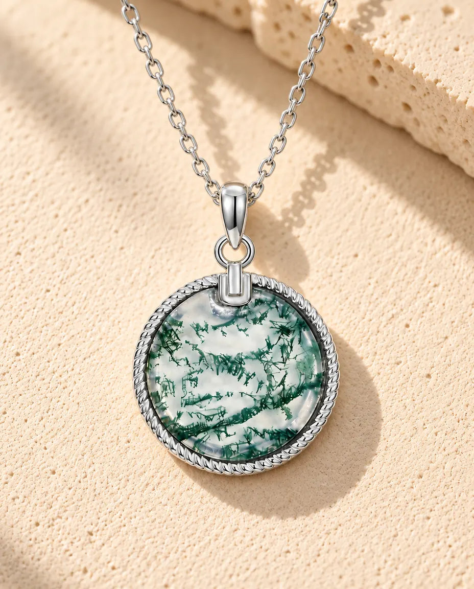 Collar de Ágata Musgosa Medallón Redondo en Plata 925 - sobre una superficie clara con textura junto a un bloque de travertino