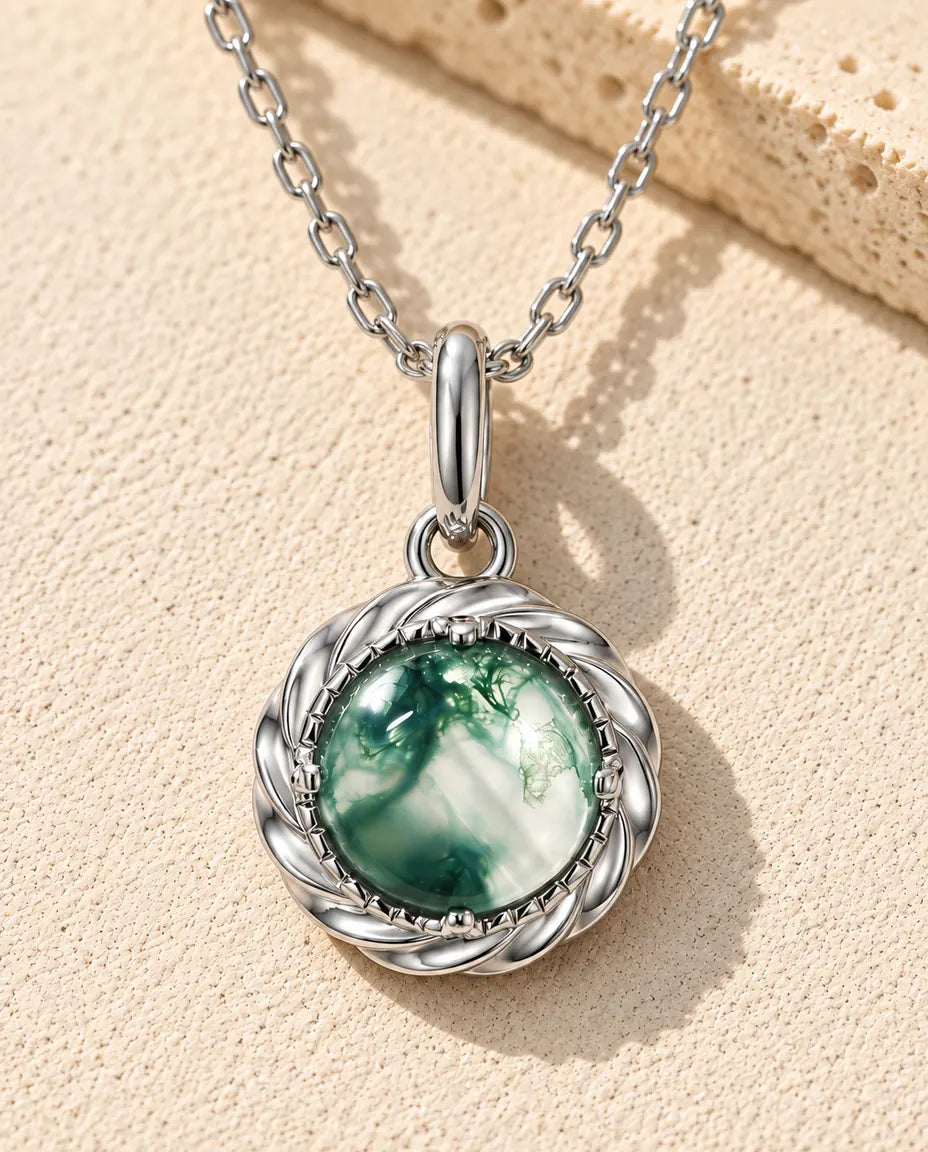 Collar con Colgante de Ágata Musgosa Redonda en Plata 925 - sobre una superficie clara con textura junto a un bloque de travertino