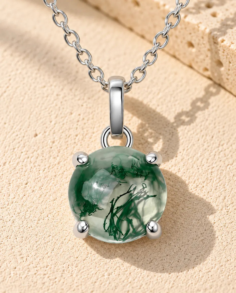 Collar de Ágata Musgosa Redonda en Plata 925 - sobre una superficie clara con textura junto a un bloque de travertino