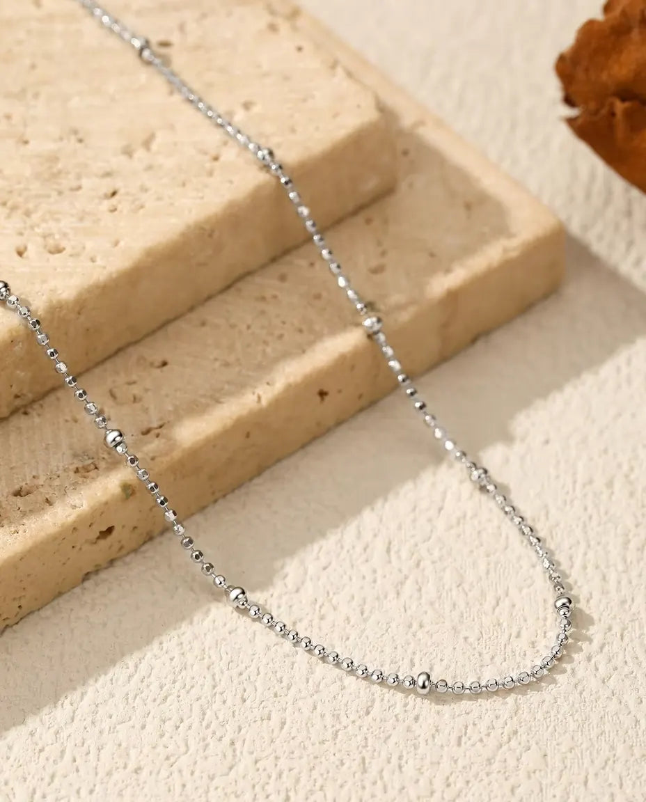 Collar Cadena con Bolitas en Plata 925 - sobre una superficie clara junto a una losa de travertino