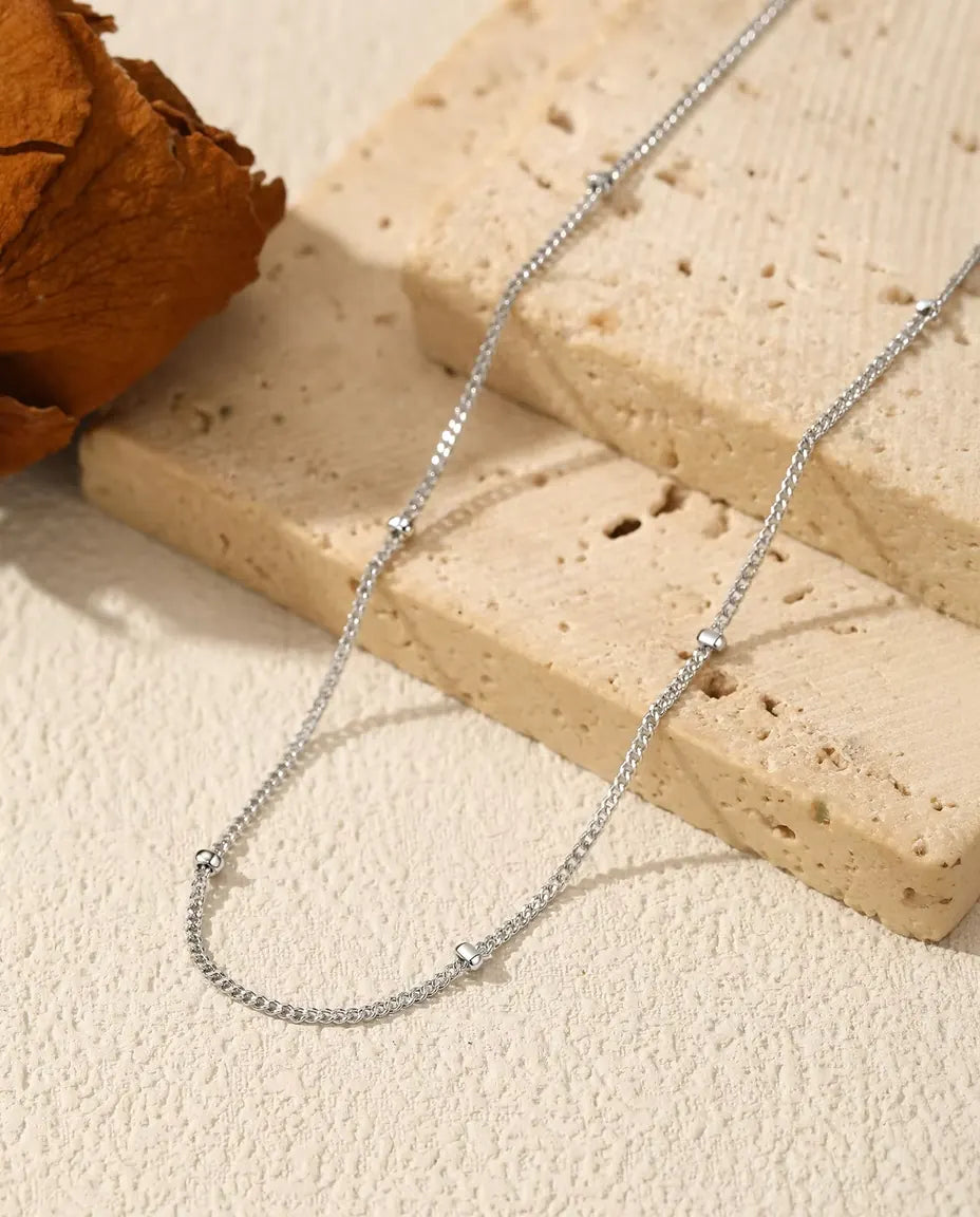 Collar Cadena Satélite en Plata 925 - sobre una superficie clara junto a una losa de travertino