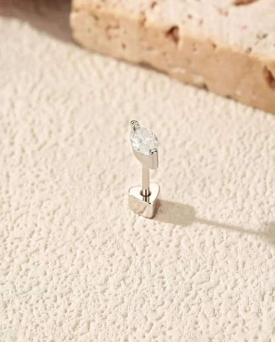 Pendientes de Moissanita Marquesa en Medio Bisel - de pie sobre su cierre en forma de corazón, en una superficie clara con textura