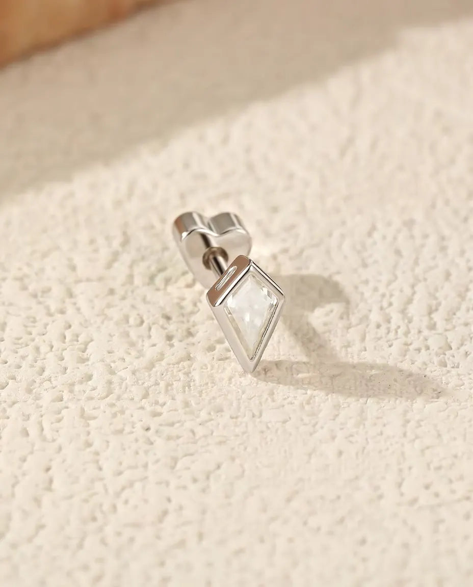 Pendientes de Moissanita Talla Cometa en Plata 925 - tumbado de lado sobre una superficie clara con textura, con el cierre en forma de corazón en el poste