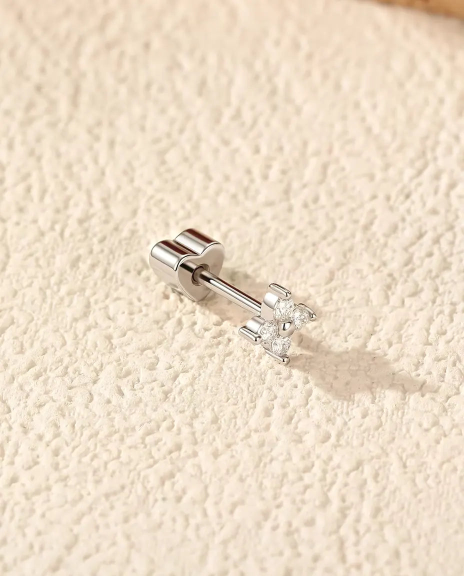 Pendientes Trébol de Cuatro Hojas de Moissanita en Plata 925 - tumbado de lado sobre una superficie clara con textura, con el cierre en forma de corazón en el poste