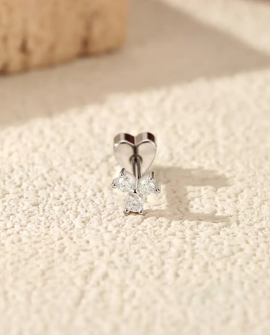 Pendientes Trébol de Moissanita en Plata 925 - de pie sobre su cierre en forma de corazón, en una superficie clara con textura