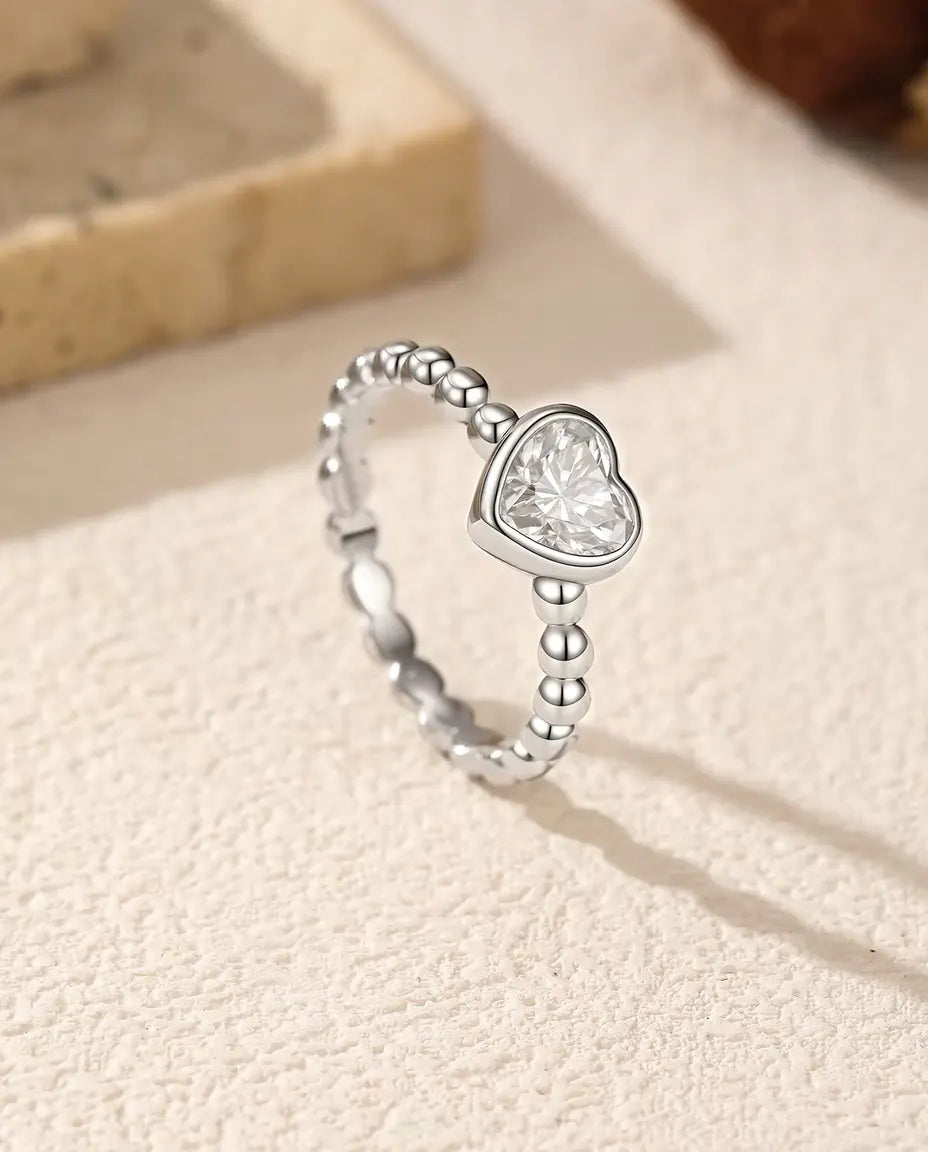 Anillo de Corazón con Moissanita en Plata 925 - de pie sobre una superficie clara con textura