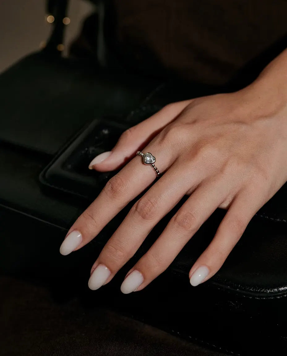 Anillo de Corazón con Moissanita en Plata 925 - llevado en una mano apoyada sobre un bolso negro
