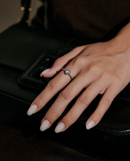 Anillo de Corazón con Moissanita en Plata 925 - llevado en una mano apoyada sobre un bolso negro