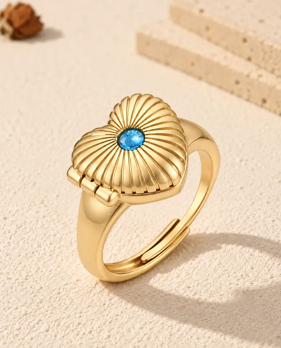 Anillo relicario de corazón con foto en color oro, con una piedra de nacimiento azul en la tapa estriada
