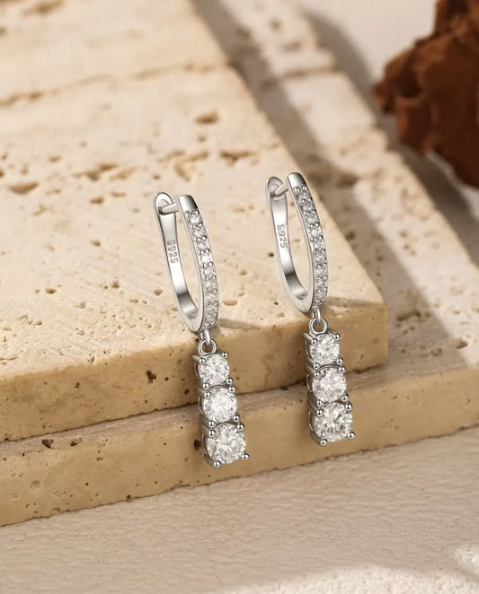 Pendientes de Aro Colgantes con Tres Moissanitas en Plata 925 - el par colgado del borde de una losa de travertino