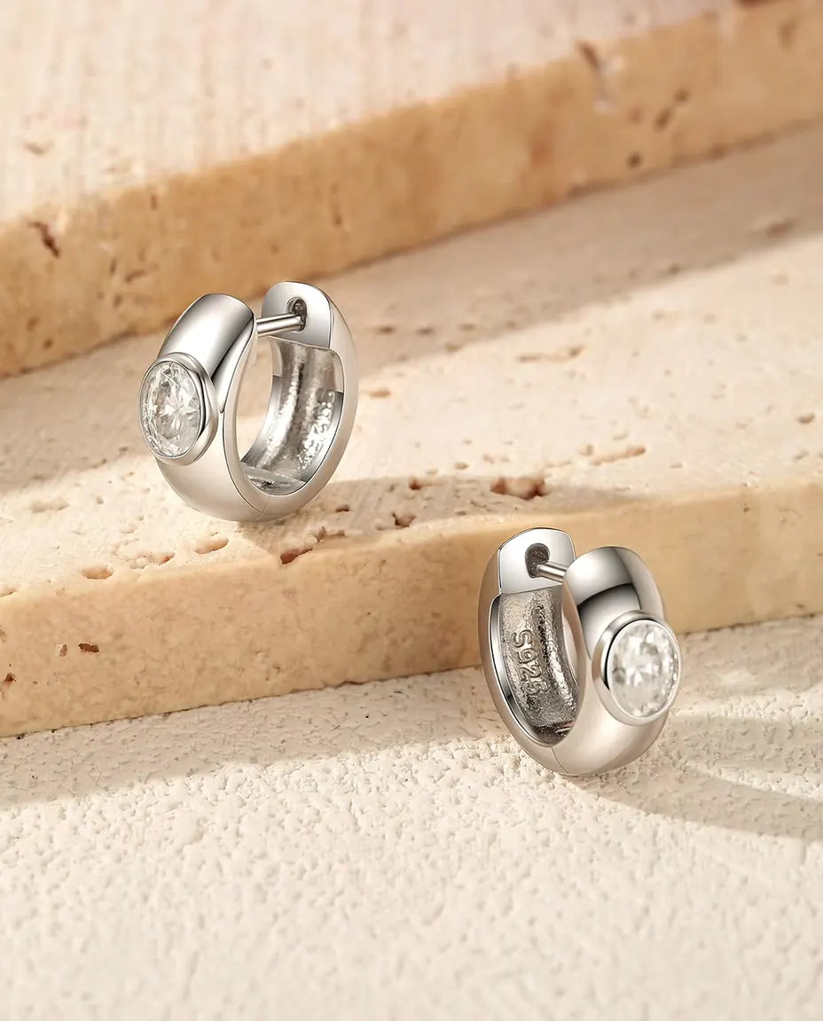 Pendientes Aro Huggie de Moissanita Oval en Plata 925 - el par sobre unos escalones de travertino