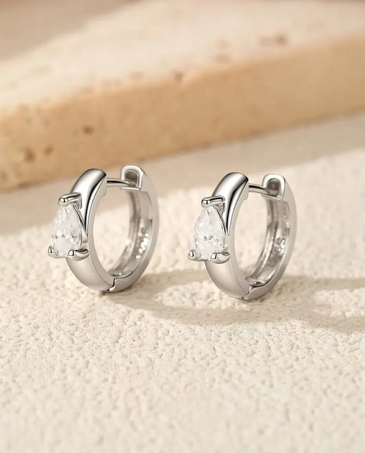 Pendientes Aro Huggie de Moissanita Pera en Plata 925 - el par de pie, uno junto al otro, sobre una superficie clara con textura