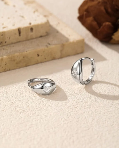 Pendientes de Aro Huggie de Moissanita Talla Asscher en Plata 925 - el par sobre una superficie clara con textura, uno tumbado y otro de pie