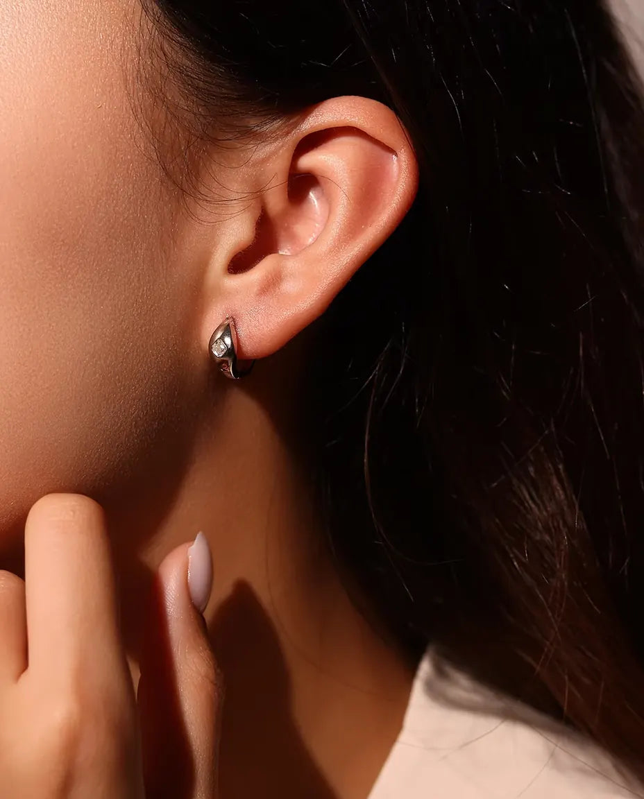 Pendientes de Aro Huggie de Moissanita Talla Asscher en Plata 925 - llevados en la oreja de una modelo, con la mano cerca de la cara