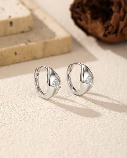 Pendientes de Aro Huggie de Moissanita Talla Asscher en Plata 925 - el par uno junto al otro sobre una superficie clara con textura