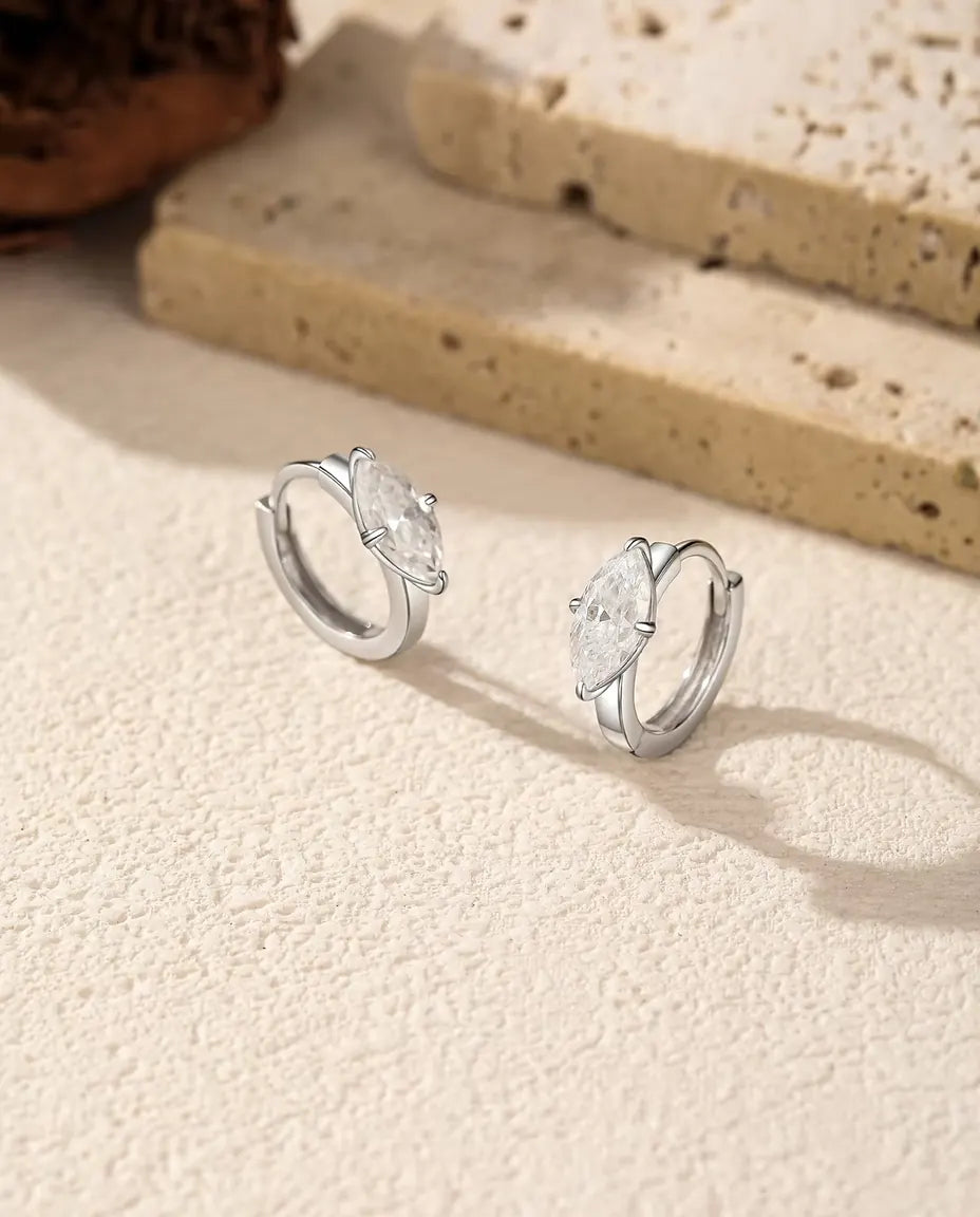 Pendientes de Aro de Moissanita en Plata 925 - el par uno junto al otro sobre una superficie clara con textura