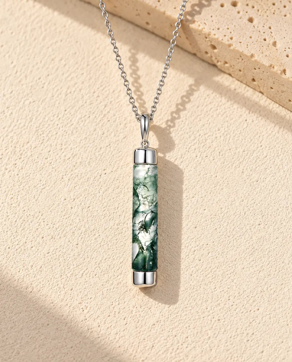 Collar de Ágata Musgosa Cilindro Largo en Plata 925 - sobre una superficie clara con textura junto a un bloque de travertino