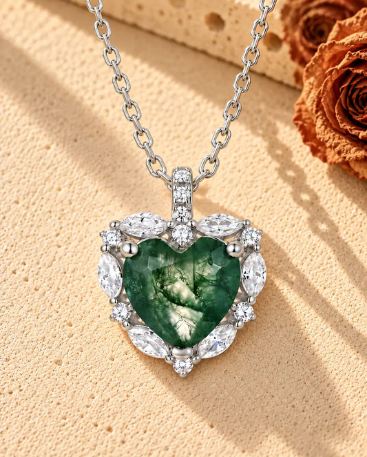 Collar de Ágata Musgosa Corazón con Halo en Plata 925 - sobre una superficie clara con textura junto a un bloque de travertino