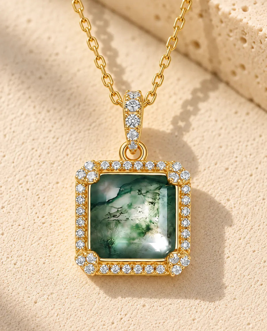 Collar de Ágata Musgosa Cuadrada en Plata 925 - versión dorada sobre una superficie clara con textura junto a un bloque de travertino