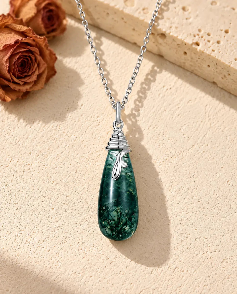 Collar de Ágata Musgosa en Forma de Gota en Plata 925 - sobre una superficie clara con textura junto a un bloque de travertino