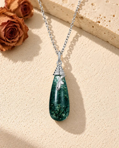Collar de Ágata Musgosa en Forma de Gota en Plata 925 - sobre una superficie clara con textura junto a un bloque de travertino