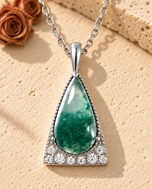 Collar de Ágata Musgosa Triángulo en Plata 925 - sobre una superficie clara con textura junto a un bloque de travertino