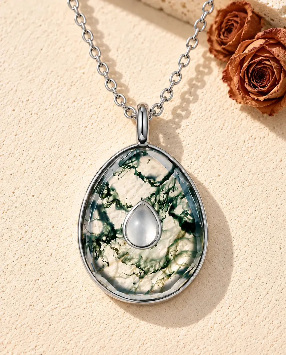 Collar de Ágata Musgosa en Forma de Huevo en Plata 925 - sobre una superficie clara con textura junto a un bloque de travertino