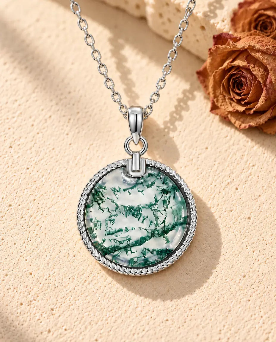 Collar de Ágata Musgosa con Colgante Redondo en Plata 925 - sobre una superficie clara con textura junto a un bloque de travertino