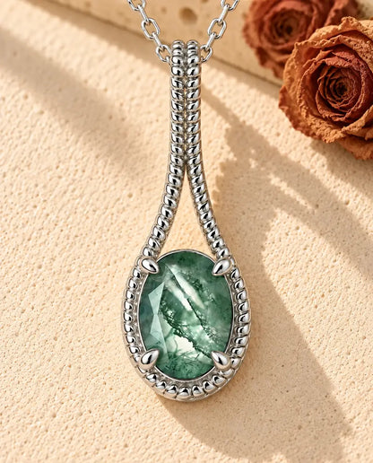 Collar de Ágata Musgosa Ovalada en Plata 925 - sobre una superficie clara con textura junto a un bloque de travertino