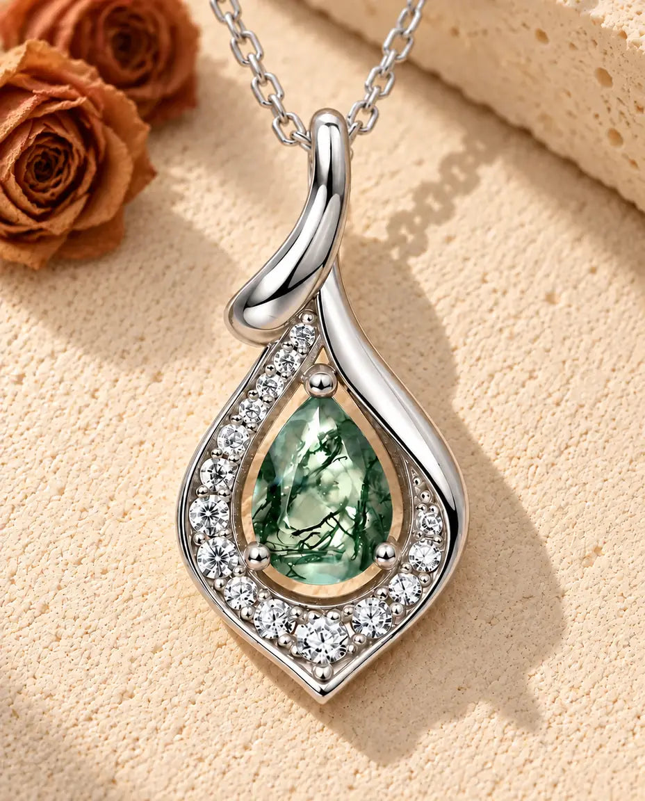 Collar de Ágata Musgosa en Forma de Pera en Plata 925 - sobre una superficie clara con textura junto a un bloque de travertino