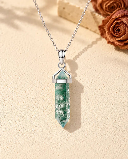 Collar de Ágata Musgosa Punta Hexagonal en Plata 925 - sobre una superficie clara con textura junto a un bloque de travertino
