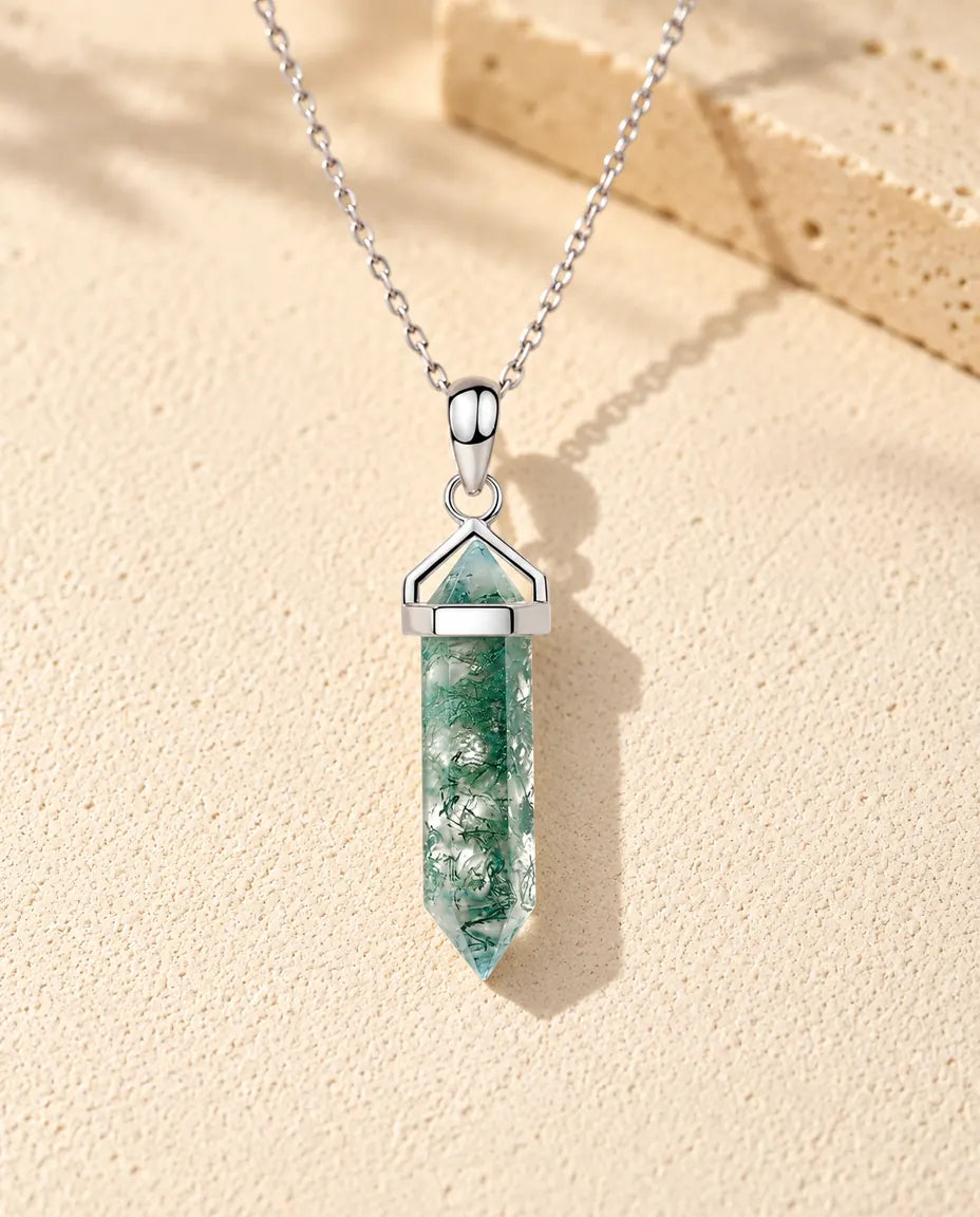 Collar de Ágata Musgosa Punta Hexagonal en Plata 925 - sobre una superficie clara con textura junto a un bloque de travertino