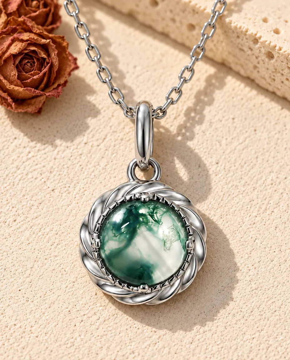 Collar con Colgante de Ágata Musgosa Redonda en Plata 925 - sobre una superficie clara con textura junto a un bloque de travertino