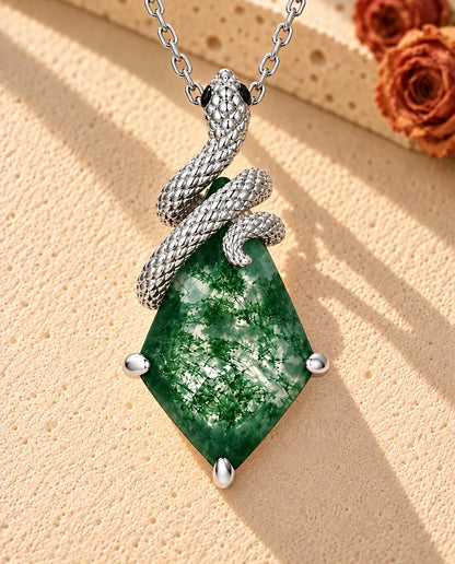 Collar de Ágata Musgosa con Serpiente en Plata 925 - sobre una superficie clara con textura junto a un bloque de travertino