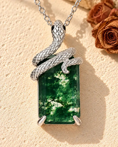 Collar de Ágata Musgosa con Serpiente en Plata 925 - sobre una superficie clara con textura junto a un bloque de travertino