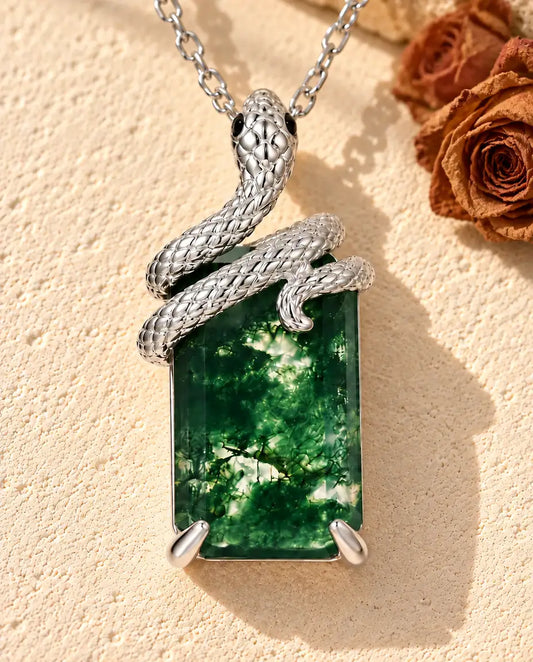 Collar de Ágata Musgosa con Serpiente en Plata 925 - sobre una superficie clara con textura junto a un bloque de travertino