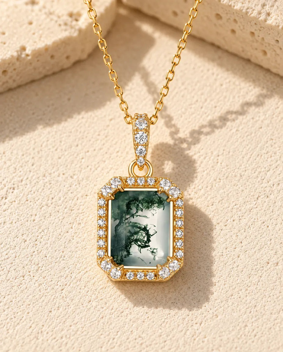 Collar de Ágata Musgosa Talla Esmeralda en Plata 925 - versión dorada sobre una superficie clara con textura junto a un bloque de travertino