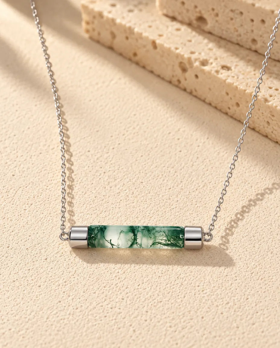 Collar de Barra de Ágata Musgosa en Plata 925 - sobre una superficie clara con textura junto a un bloque de travertino