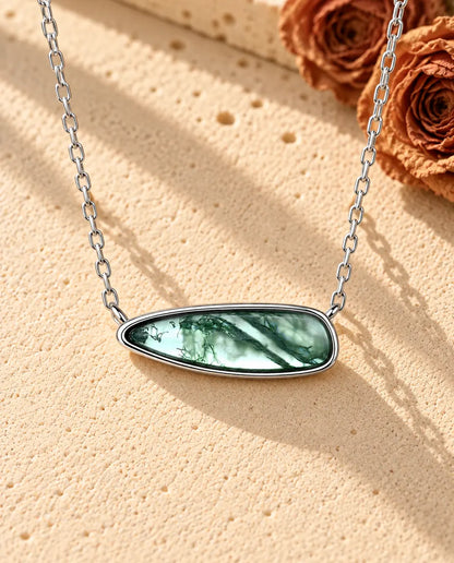 Collar Barra de Ágata Musgosa en Plata 925 - sobre una superficie clara con textura junto a un bloque de travertino