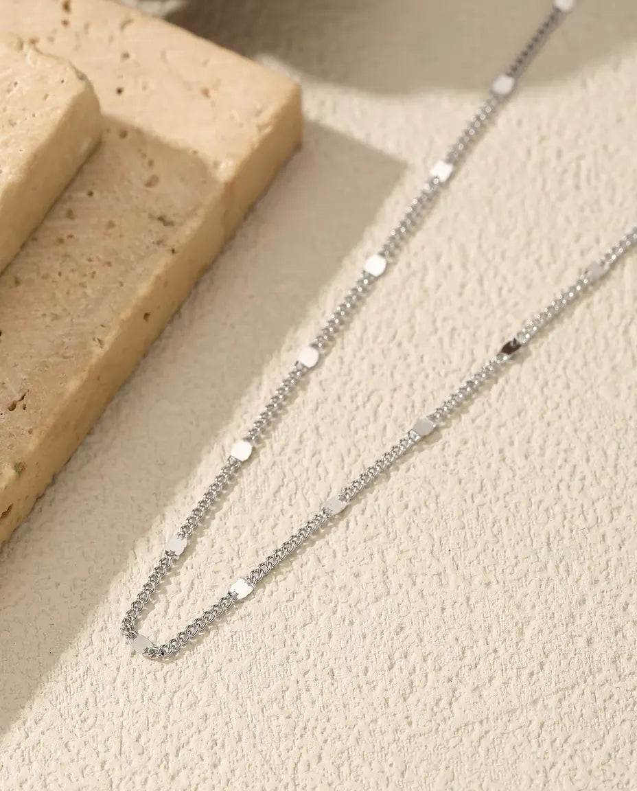 Collar de Cadena con Óvalos en Plata 925 - sobre una superficie clara junto a una losa de travertino
