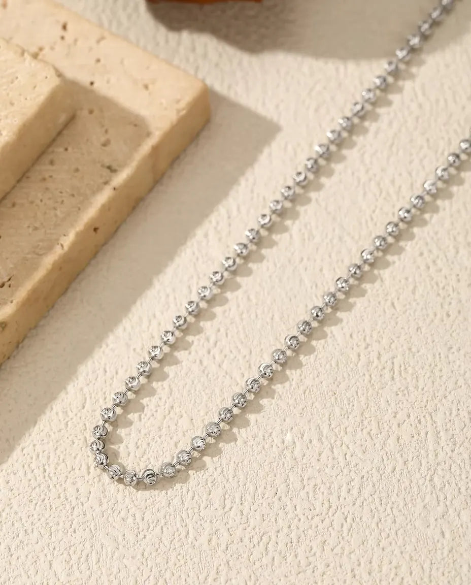 Collar de Bolitas Facetadas en Plata 925 - sobre una superficie clara junto a una losa de travertino