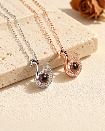 Collares de cisne con foto dentro en plateado y en color oro rosa, tumbados sobre yeso
