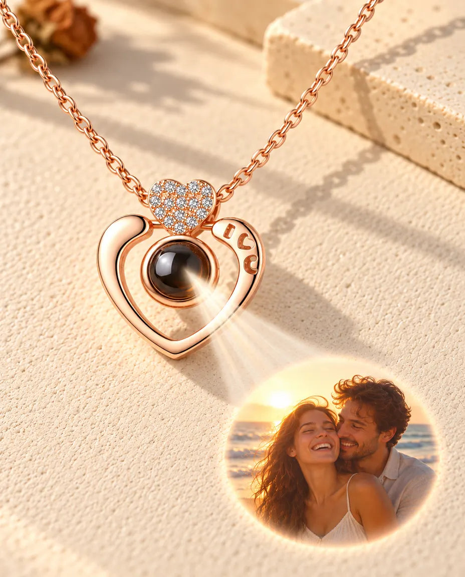 Collar de corazón abierto en color oro rosa cuya bola muestra una foto de pareja en la playa sobre yeso crema