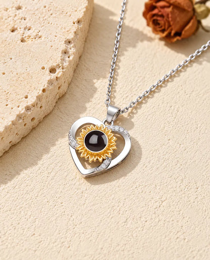 Collar con foto dentro de corazón con girasol dorado, apoyado sobre una losa de travertino
